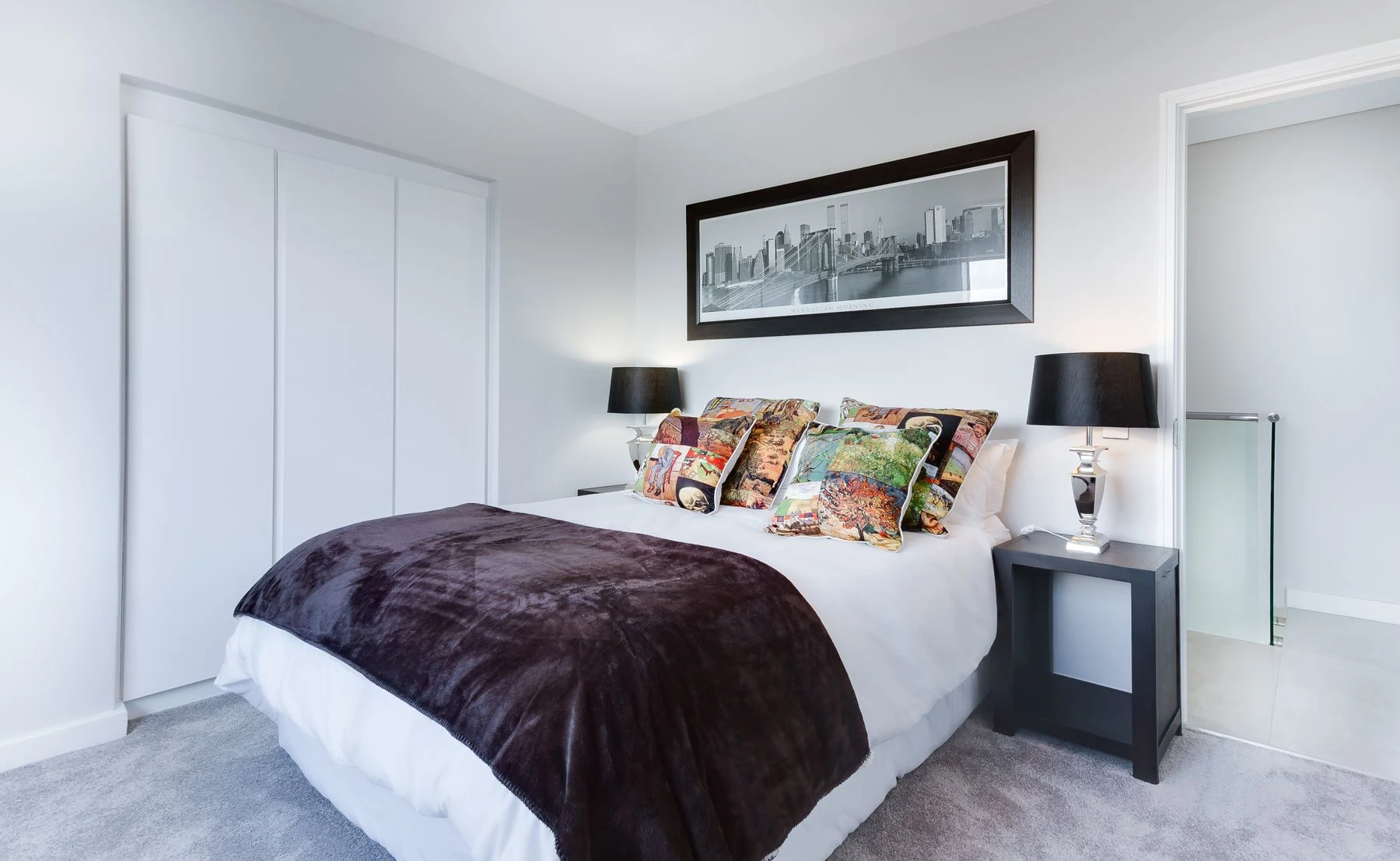 Stylish and contemporary bedroom featuring a cityscape artwork, colorful pillows, and modern decor. Reference photograph for Nocturne House.
