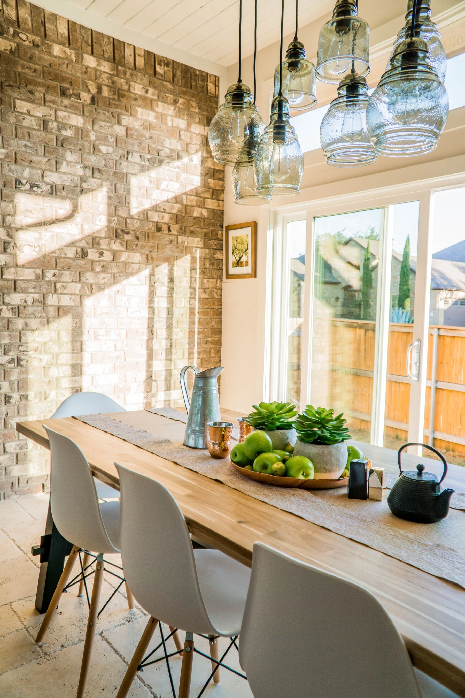 Sunlit dining room with contemporary decor and a rustic brick wall, featuring stylish lighting and a wooden table. Reference photograph for Atelier Sora.