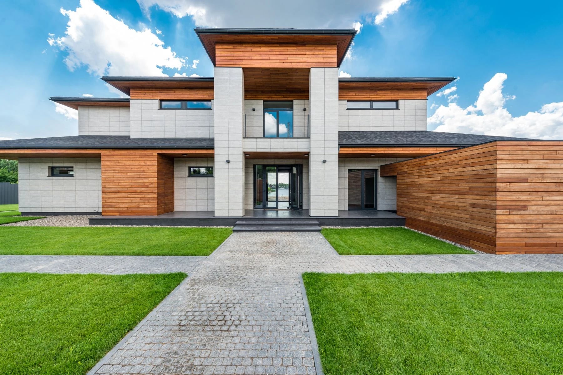 Contemporary house with wood and stone facade set against a vibrant blue sky. Reference photograph for Sela Residence.