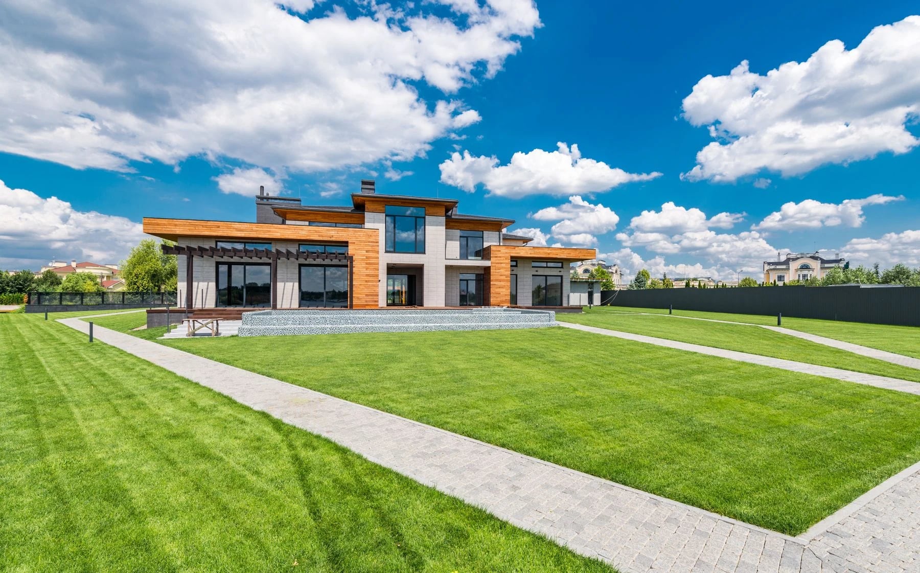 A contemporary villa surrounded by lush green lawn under a bright blue sky. Reference photograph for Sela Residence.